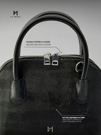Black handbag with double zipper closure on a gray background, featuring Le Mesh branding.