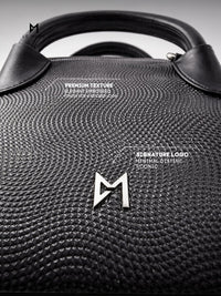 Black textured handbag with a brand logo on a gray background