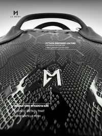 Black textured leather bag with 'M' logo and brand name 'Le Mesh' on a gray background